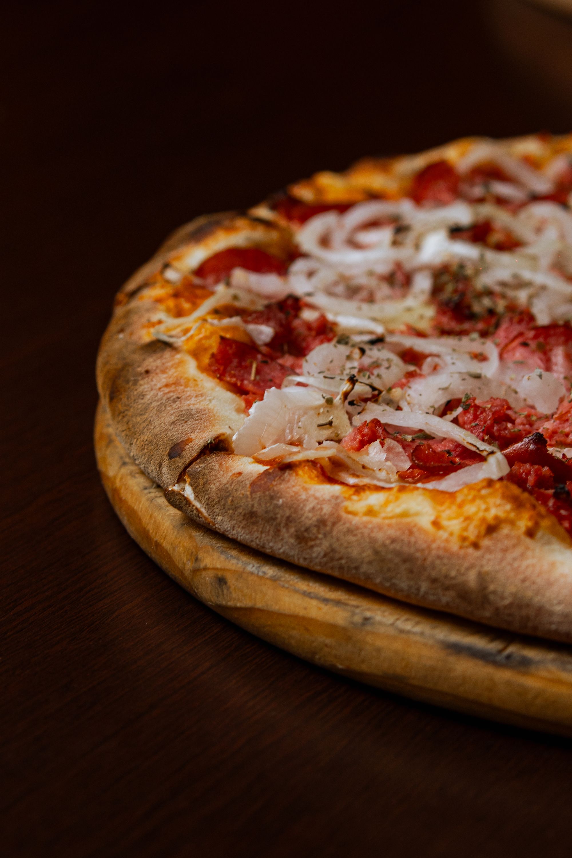 Pizza com linguiça, cebola e borda dourada sobre uma tábua de madeira